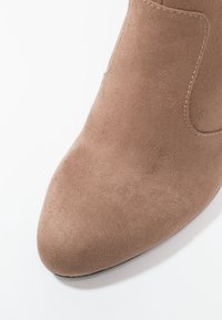 Světle hnědá semišová kotníková bota se špičatou špičkou a prošitými detaily. Hladká textura a minimalistický design. Plochá gumová podrážka.