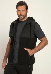 Schwarze Fleece-Weste mit einem Reißverschluss und Kapuze, ausgestattet mit einem einfarbigen Oberteil und zwei Seitentaschen, getragen über einem dunkelgrauen Hemd.