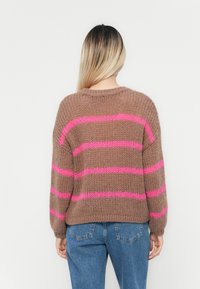 Brązowy sweter pleciony z różowymi poziomymi paskami, z okrągłym dekoltem i luźnym krojem, zestawiony z niebieskimi spodniami o wysokim stanie.