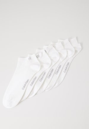 Sechs Paar weiße Socken mit Knöchelschnitt, auf denen "Calvin Klein" in Grau an den Seiten gedruckt ist, überlappend auf einem weißen Hintergrund angeordnet.