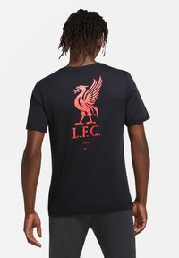 Czarna bawełniana koszulka z wyraźnym czerwonym logo Liverpool i tekstem na plecach. Krótkie rękawy i klasyczny okrągły dekolt.