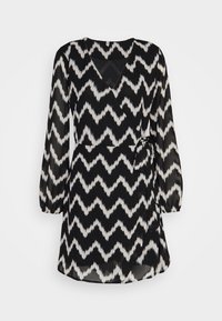 Svart och vit zigzag-mönstrad omlottklänning med långa ärmar, tillverkad av lätt tyg, med en knytning i midjan och en V-ringning.