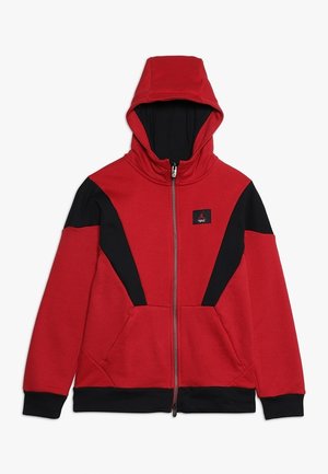 Sudadera con capucha roja y negra con cremallera, cuello alto, bolsillos frontales, paneles en contraste y un logo en el pecho. Textura suave, diseño deportivo.