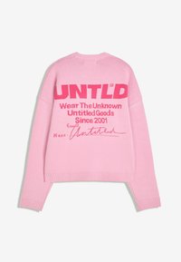 Roza dolgi rokav pleten pulover z rdečim besedilom "UNTLD," "Nosite neznano" in "Nepodpisane dobrine od 2001" na hrbtu.