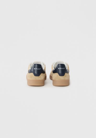 Baskets en suède beige avec un empiècement de talon en cuir bleu marine. Elles présentent un logo blanc, une semelle en caoutchouc et un design classique bas.