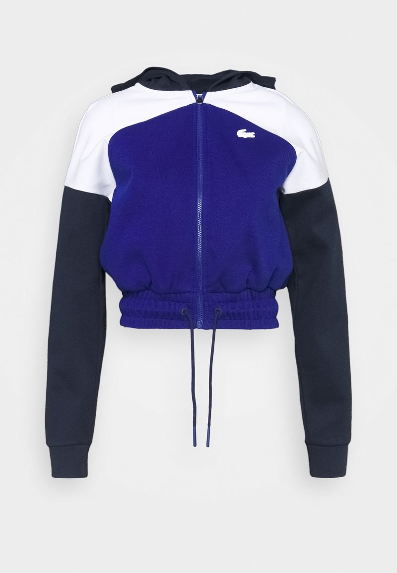 Gehaakte hoodie met ritssluiting in paars, marineblauw en wit. Voorzien van een nauwsluitende taille, capuchon en logo op de borst. Zachte textuur, sportief ontwerp.