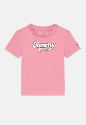 T-shirt en coton rose à manches courtes, col rond, avec un logo brodé blanc portant l'inscription "Tommy CLASS OF 1985" sur le devant.