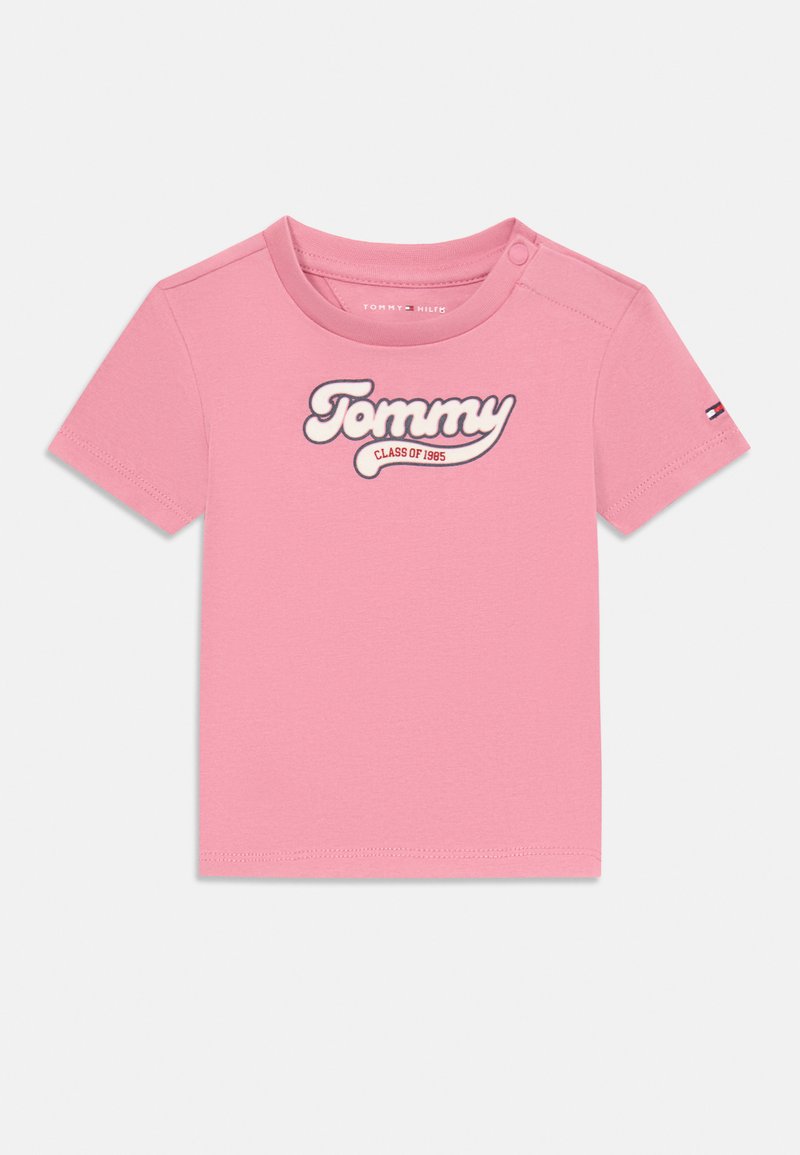 T-shirt in cotone rosa con maniche corte, scollatura rotonda e un logo ricamato bianco che recita "Tommy CLASS OF 1985" sul davanti.