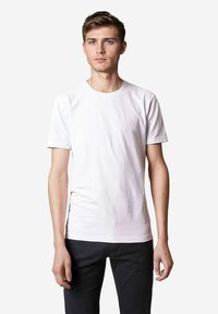 Weißes Baumwoll-T-Shirt mit Rundhalsausschnitt und kurzen Ärmeln, das eine glatte Textur und einen figurbetonten Schnitt aufweist, kombiniert mit dunklen Jeans.