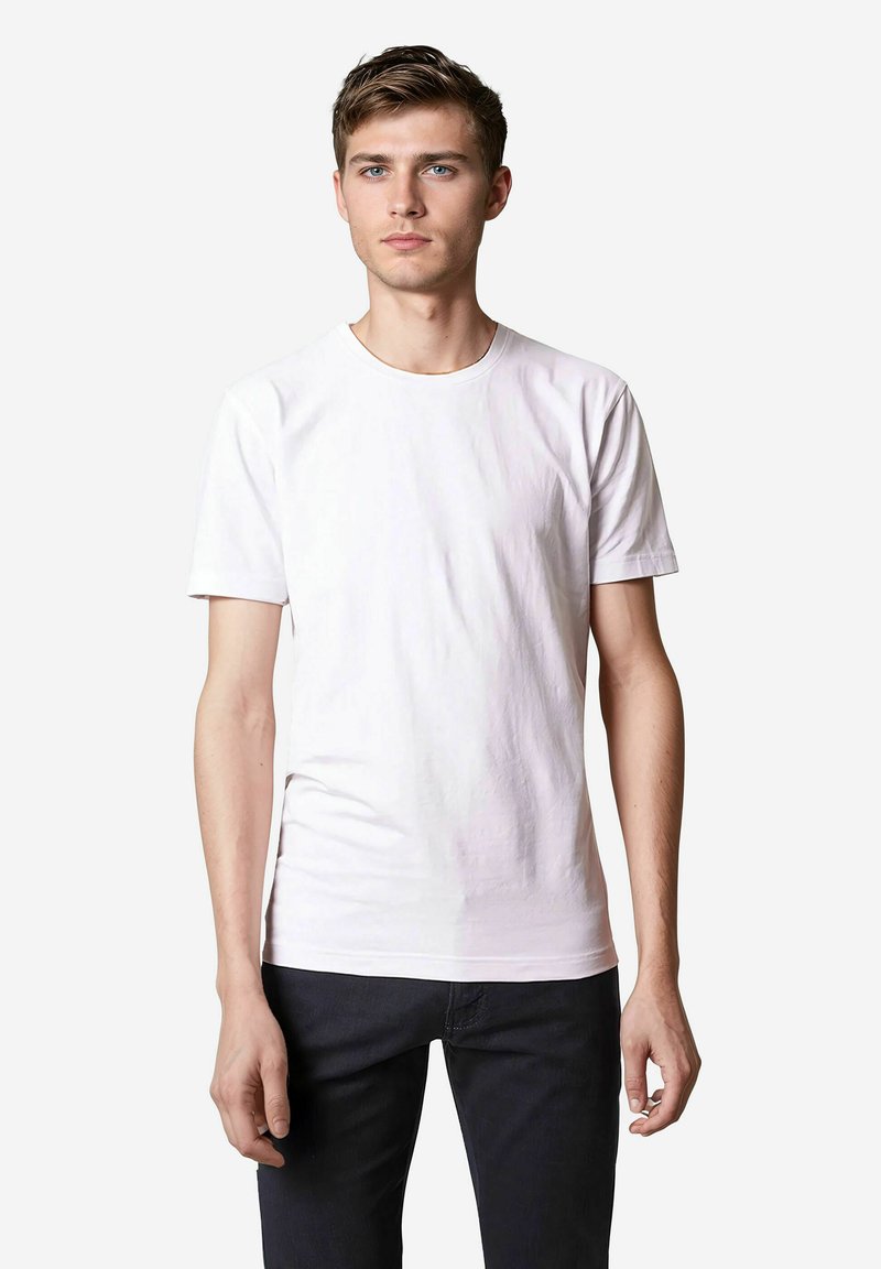 Weißes Baumwoll-T-Shirt mit Rundhalsausschnitt und kurzen Ärmeln, das eine glatte Textur und einen figurbetonten Schnitt aufweist, kombiniert mit dunklen Jeans.