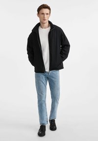 Czarna, lekka kurtka zapinana na zamek, lekko teksturowana, z kołnierzem stojącym, zestawiona z białą koszulką i jasnoniebieskimi dżinsami.