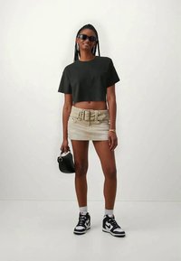 Tricou scurt negru, fustă mini din denim bej cu un curea groasă, geantă neagră și adidași alb-negru cu șosete albe.
