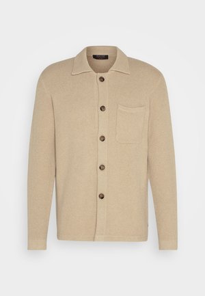 Bežinis megztas kardiganas su apykakle, septyniais mygtukais ir krūtinės kišene. Audinys su tekstūra ir ilgomis rankovėmis su paprastais rankogaliais.