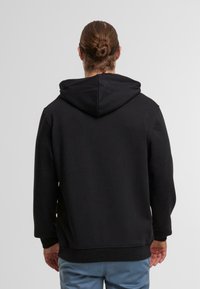 Czarna bluza z kapturem o luźnym kroju, teksturowana tkanina, ściągacze przy rękawach i na dole. Brak widocznych logo i wzorów.