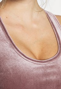 Top in velluto di un rosa tenue con un ampio scollo e una texture liscia; evidenzia una sottile lucentezza e una silhouette curvata.