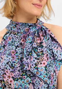 Haut halter fleuri avec un fond noir, comportant un mélange de fleurs violettes, bleues et roses. Tissu doux, détail de lien au cou.
