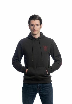 Haut à capuche noir avec cordons de serrage et une poche avant. Présente un graphique rouge sur la poitrine. Associé à un jean en denim bleu.