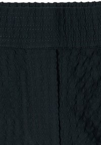 Gros plan sur un tissu noir froissé avec des coutures horizontales et une ceinture élastique, montrant la texture et les détails de la couture.