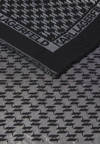 Sort og sølv tørklæde med et gentagende logo-mønster, frynsekant og en glat, struktureret overflade. Mål ca. 70x70 cm.