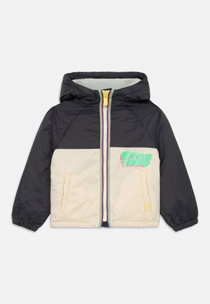 Padded jacket with a black upper and cream lower section, featuring a multi-colored zipper and “NEVER TIRED” graphic on the front.