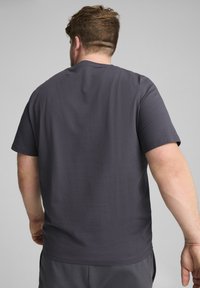 Mørkegrå kortærmet t-shirt med et enkelt design og glat tekstur, set fra ryggen. Rund hals og afslappet pasform.