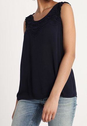 Mouwloos nachtblauw topje met kanten detail langs de halslijn, gedragen met lichtblauwe spijkerbroek op een staande persoon.