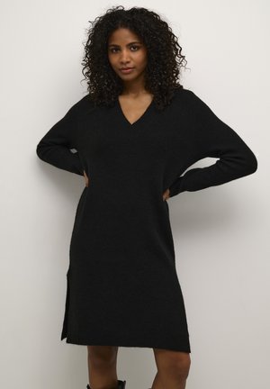 Robe tricotée noire à col en V avec des manches longues, des fentes sur les côtés et une coupe ample, fabriquée en tissu texturé doux.
