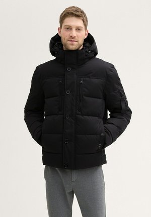 Schwarze Pufferjacke mit hohem Kragen, mit einem durchgängigen Reißverschluss, mehreren Reißverschlusstaschen und einer abnehmbaren Kapuze; gestepptes Design.