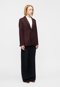 Μπορντό σακάκι ραμμένο στα μέτρα με πέτο με εγκοπές, δύο τσέπες, φορεμένο πάνω από άσπρο πουκάμισο. Συνδυασμένο με φαρδιά μαύρη παντελόνια και καφέ μοκασίνια.