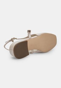 Scarpa in pelle verniciata nuda con cinturino alla caviglia regolabile, tacco a blocco e suola in gomma testurizzata. Finitura liscia con minime accentuazioni hardware.