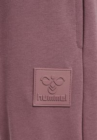 Lila Hummel-Sweatshirt mit strukturiertem Stoff, geripptem Muster und einem auffälligen, geprägten Logopatch mit geometrischem Design.