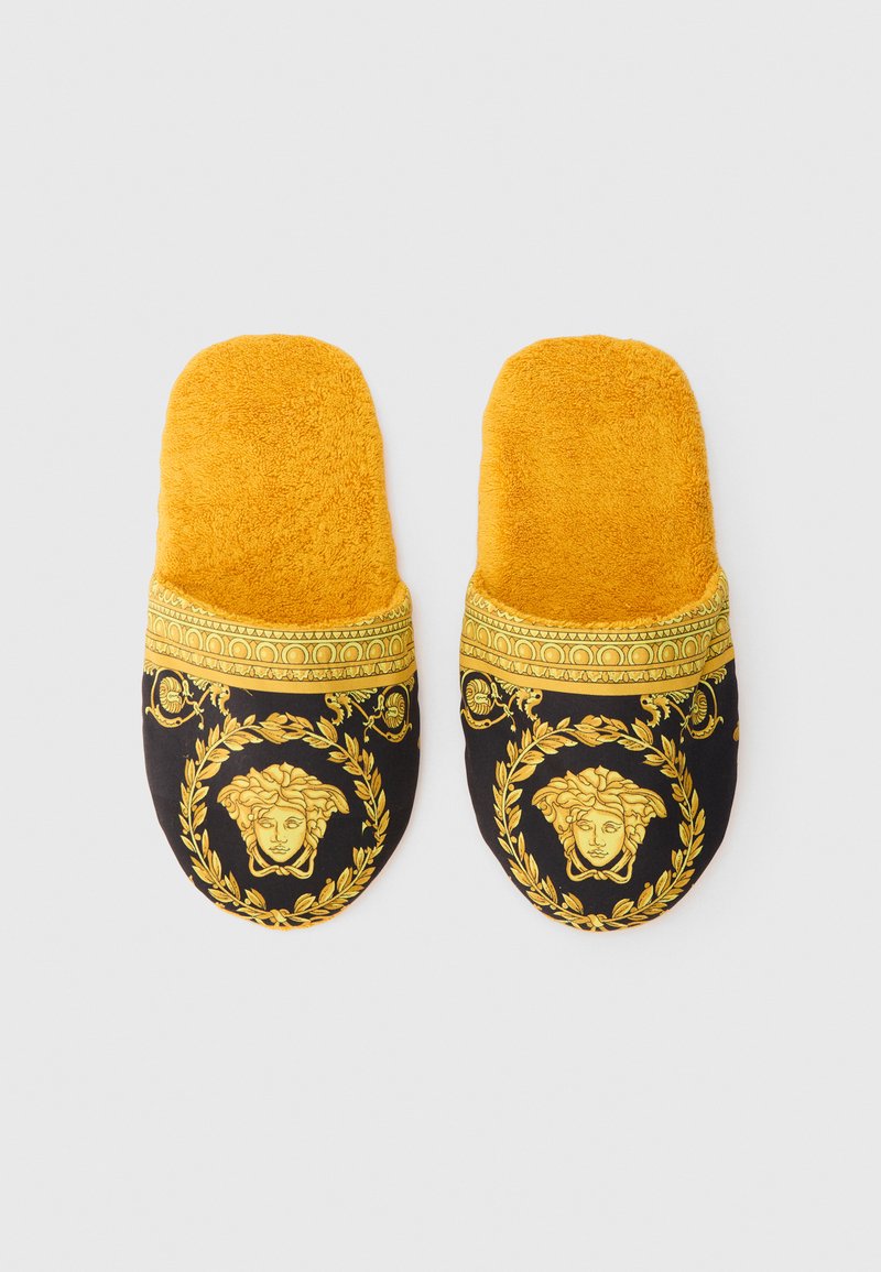 Pair of yellow and black plush slippers with gold Medusa head and ornate laurel wreath design on the toe area.