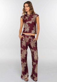 Conjunto burdeos que incluye una blusa sin mangas con cuello alto y pantalones de pierna ancha. Patrones florales dorados sobre un tejido texturizado.