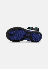 Sandalias deportivas negras y moradas con suela de goma texturada, correas ajustables y punta reforzada. Presentan detalles en acento verde.