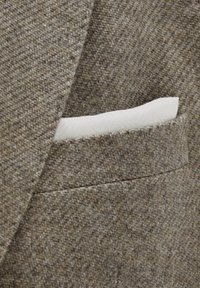 Brown textured herringbone blazer pocket with a white patterned pocket square neatly folded inside.
