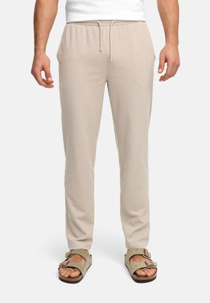 Mann trägt hellbeige strukturierte Jogginghosen mit elastischem Bund und Kordelzug, kombiniert mit beigen Sandalen mit Schnalle.