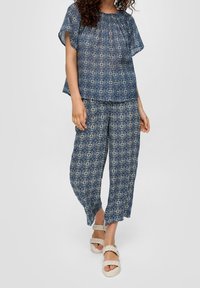 Ensemble bleu marine à motif comprenant un haut ample à manches courtes et un pantalon à coupe décontractée avec un design géométrique, associé à des sandales de couleur claire.