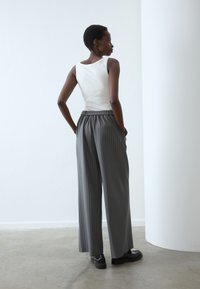 Un débardeur blanc, un pantalon large à rayures grises avec une taille ajustée et des poches latérales, associé à des chaussures noires. Vue de dos.
