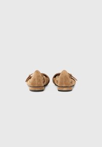 Čevlji loaferji iz semiša v svetlo rjavi barvi z ostrimi konicami, zloženi tkaninski detajl na zadnjem delu in nizka, kontrastna črna podplat.