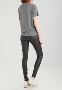 Camiseta gris de manga corta combinada con pantalones negros ajustados y zapatillas blancas. Los pantalones tienen una textura suave y detalles de costura sutiles.