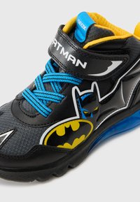 Svart sportssko med blå snørebånd, gummisåle og gule detaljer. Har Batman-logo og karakterdesign på siden. Geox-merke tydelig synlig.