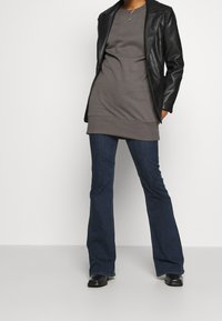 Grå långärmad topp lagd under en svart läderjacka, tillsammans med utsvängda mörkblå jeans och svarta ankelstövlar. Enkel design och texturer.