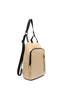 Bežový batoh s mäkkou textúrou a čiernymi popruhmi a zipsami. Obsahuje prednú kapsu na skladovanie. Kompaktný, obdĺžnikový dizajn.