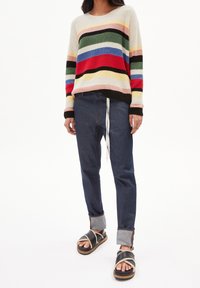 Pull tricot rayé avec des couleurs variées, coupe décontractée. Associé à un jean foncé et des sandales noires avec une sangle texturée.