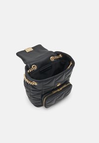 Sac à dos en cuir noir matelassé avec bretelles en chaîne dorée, poche avant zippée et compartiment principal ouvert avec rabat et fermeture par boucle.