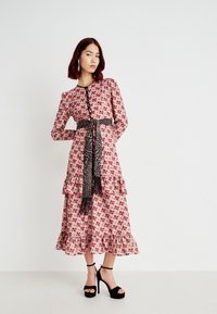 Φλοράλ φόρεμα από ροζ ύφασμα με μαύρες λεπτομέρειες, διαθέτει μακρ�ιά μανίκια, ραμμένα φουσκωτά και ζώνη με λεοπάρ μοτίβο. Μαύρες ψηλοτάκουνες γόβες.