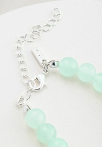 Silver chain bracelet with a lobster clasp and smooth round light green beads on a white surface.
