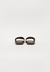 Sandali in pelle marrone con suole piatte, caratterizzati da cinturini incrociati e una texture liscia. Design minimalista e schema di colori sobrio.