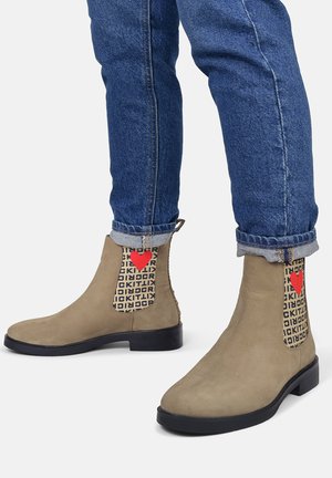 Beige Wildleder-Ankle Boots mit einer runden Zehenpartie, schwarzer Gummisohle und gemusterten Einsätzen mit einem roten Herzdesign. Erhöhter Absatz.