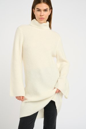 Knit turtleneck sweater in off-white, featuring long bell sleeves, textured pattern, and side slits for ease of movement.